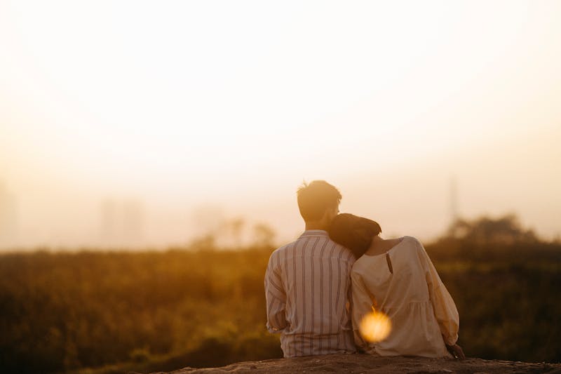 A couple sitting close together in soft warm light, leaning gently on each other in a quiet, intimate moment